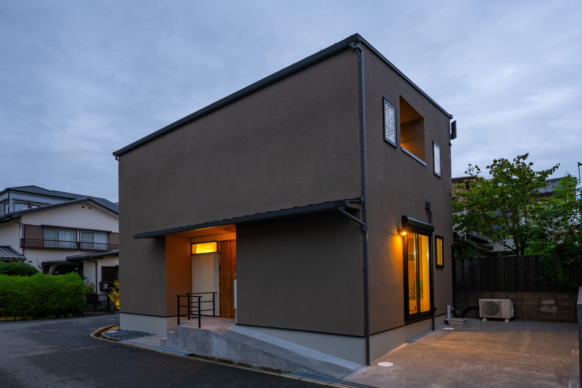 夕暮れ時に温かみのある玄関ポーチの明かりが灯る、落ち着いた佇まいのモダンな外観の住宅